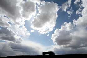 This is picture of a long distance hauling truck with a bright cloud covered skyline.